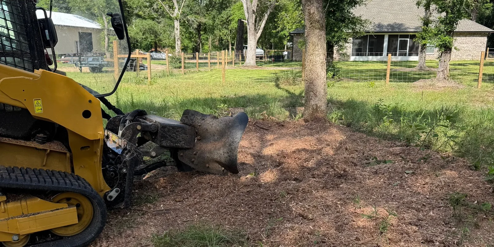 Track machine with a root grapple working freshly grubbed dirt on a residential lot near a fence line
